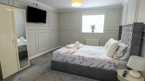 Une chambre à coucher comprenant un lit, une télévision, une fenêtre, un miroir et une table de chevet avec une lampe.