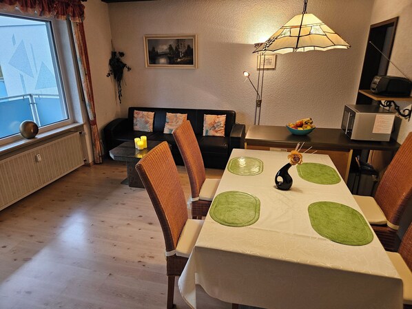 Et spiseområde med et bord dækket til fire personer, en sofa, en radiator og en lampe.