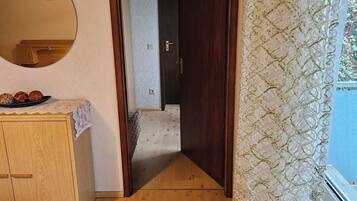 Ein Schlafzimmer mit einem Holzkoffer, einem Bett mit weißer Bettdecke und einem Fenster mit Spitzenvorhängen.