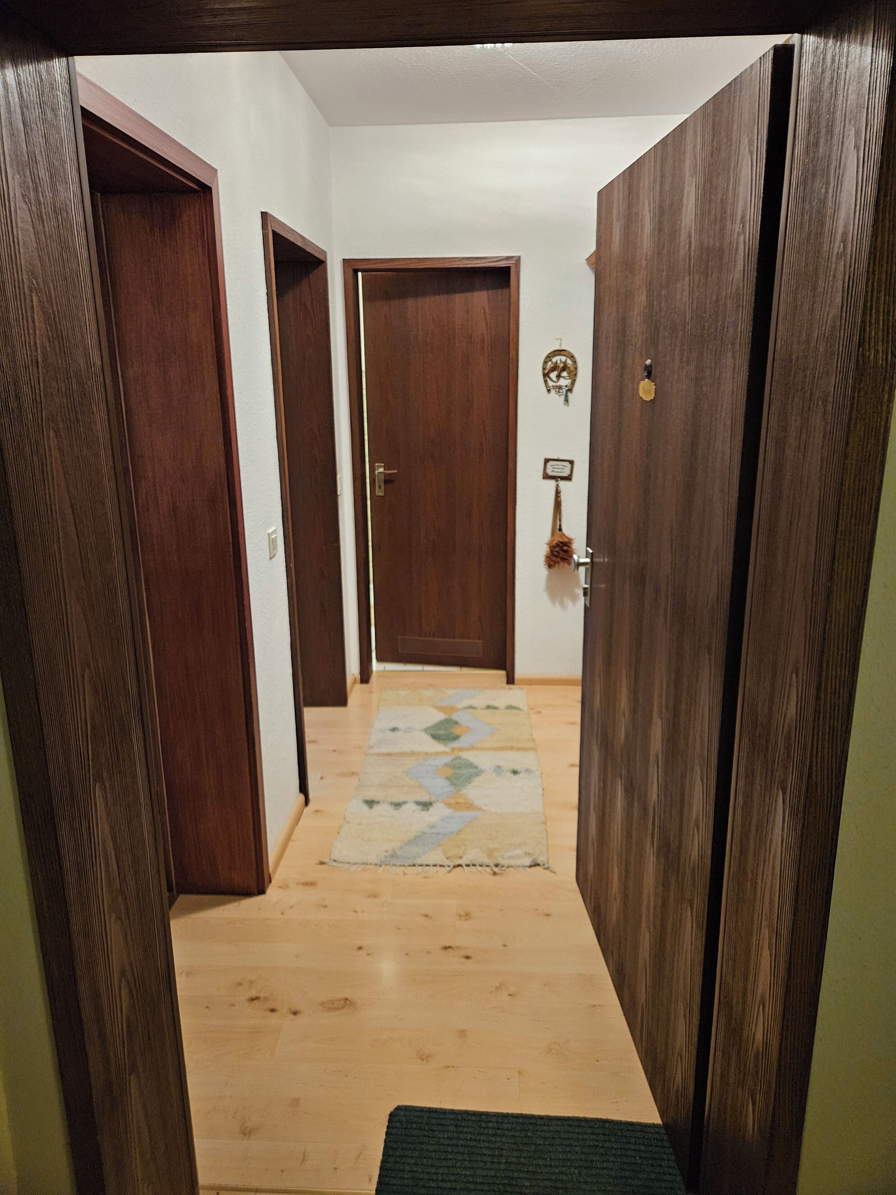 A hallway with wooden doors, a patterned rug, and a small wall decoration.