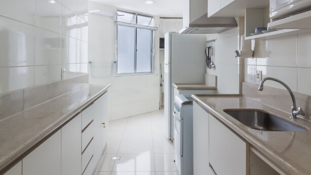 A modern kitchen with white cabinets, a stainless steel sink, and a built-in oven. - Comfort 4 minutes from Leblon Beach | AP801 (Rio de Janeiro)