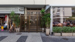 A storefront with a metal gate, potted plants, and a tiled pavement. - Comfort 4 minutes from Leblon Beach | AP801 (Rio de Janeiro)