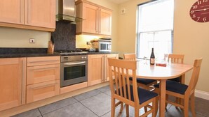A kitchen with wooden cabinets, a stove, and a dining table with chairs. - Churchside (Alnwick)