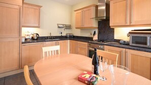 A modern kitchen with wooden cabinets, a gas stove, a microwave, and a dining table with chairs. - Churchside (Alnwick)