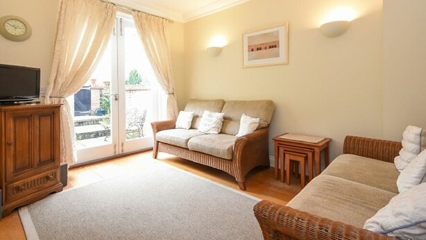 A cozy room with a large bed, a wicker sofa, a small table, a television, and a door leading to an outdoor area. - Churchside (Alnwick)