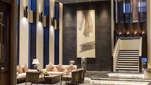A modern lobby with a sofa, chairs, a coffee table, a large abstract painting, and a staircase. - Dongya Hotel (Qingyang)