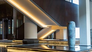 A modern lobby with a reflective floor, a central column, and a staircase with illuminated edges. - Dongya Hotel (Qingyang)