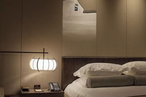 Habitación de hotel con cama, mesita de noche, lámpara y aplique de pared.