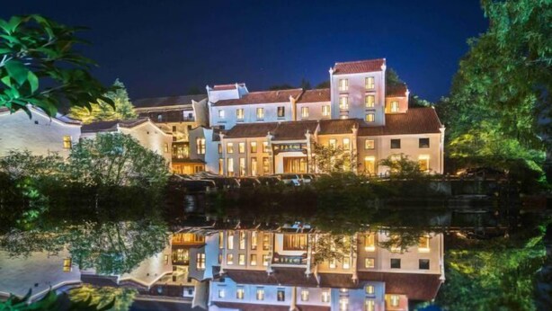 A large, multi-story hotel with a reflection in the water, featuring a mix of traditional and modern architecture. - Dongya Hotel (Qingyang)