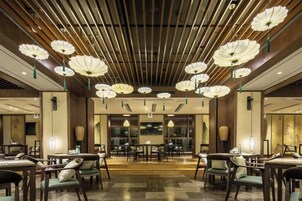 Un comedor espacioso con varias mesas y sillas, techo de madera con lámparas colgantes, y vista del comedor a través de grandes ventanales.
