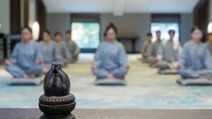 A group of people seated in a row, meditating in a room with a patterned floor and a decorative object in the foreground. - Dongya Hotel (Qingyang)