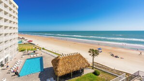 A hotel with a pool, beach view, and a thatched-roof structure.