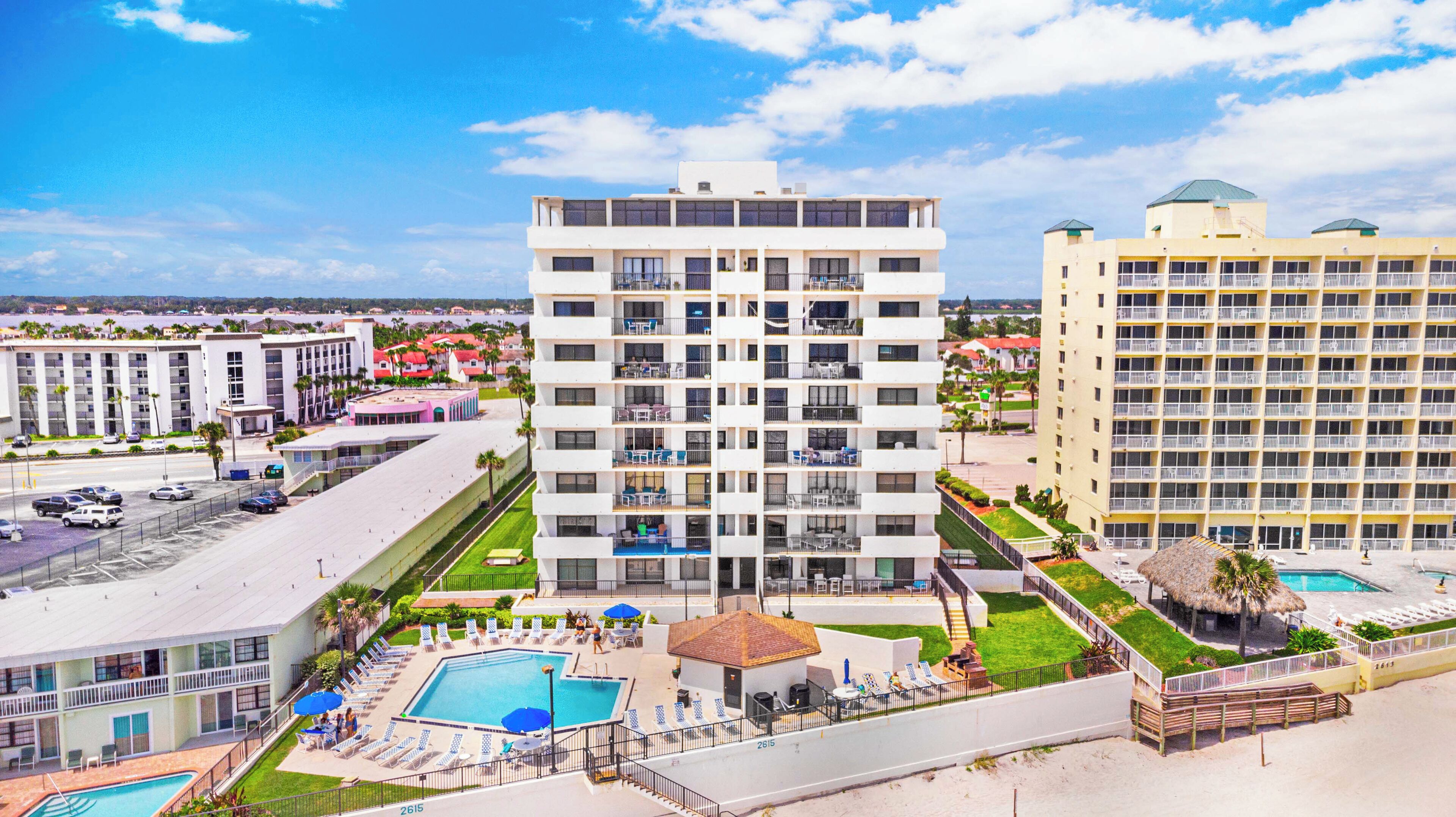 Un hotel con varios pisos, piscina al aire libre y zona de playa con sillas y sombrillas.