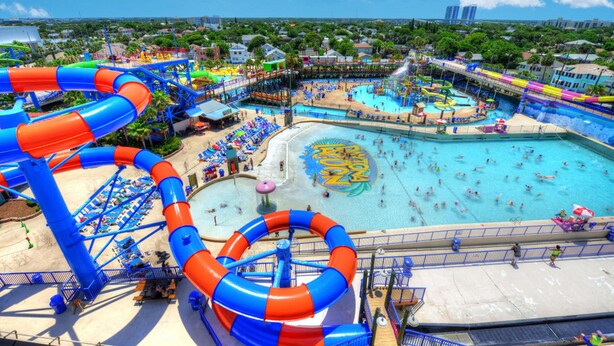 A water park with multiple slides and pools, surrounded by beach areas and lounge chairs.