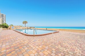 Ein Pool mit Fliesen umgeben, eine Palme und ein Strand im Hintergrund.