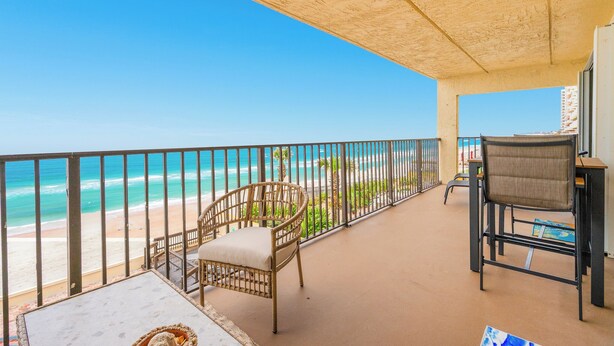 A balcony with a view of the beach and ocean, a wicker chair, and a table with a basket. - Oceanfront | No-drive Beach | Sea Fern #303 (Daytona Beach Shores)