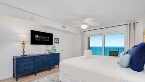A bedroom with a large bed, a ceiling fan, a TV on the wall, and a view of the ocean. - Oceanfront | No-drive Beach | Sea Fern #303 (Daytona Beach Shores)