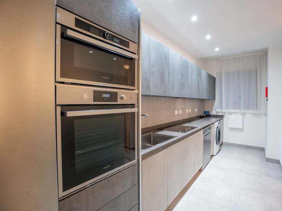 A modern kitchen with stainless steel appliances, a built-in oven, a microwave, a dishwasher, and a large window with curtains.