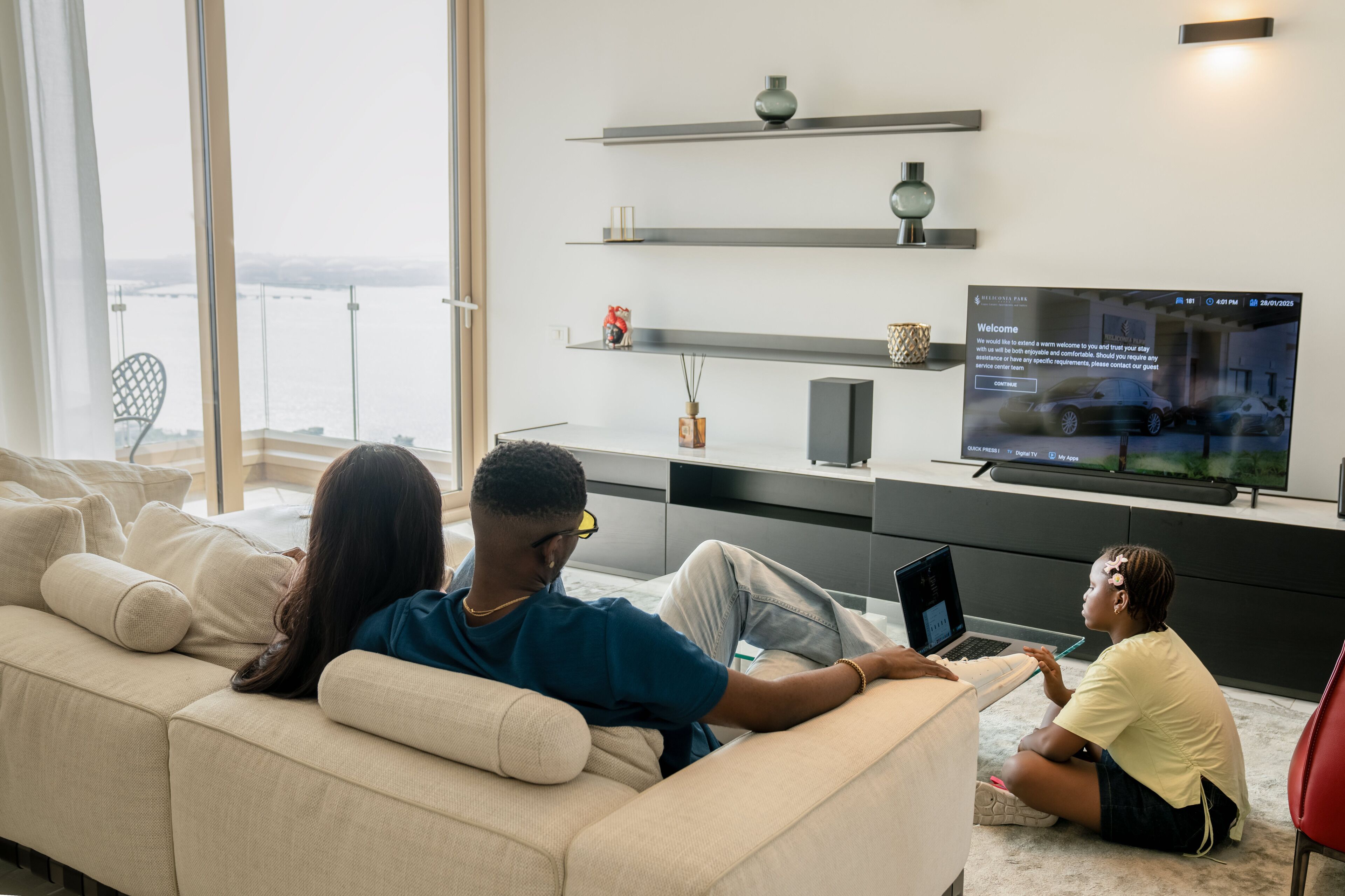 Un salon moderne avec un grand téléviseur à écran plat, un canapé et une personne utilisant un ordinateur portable.