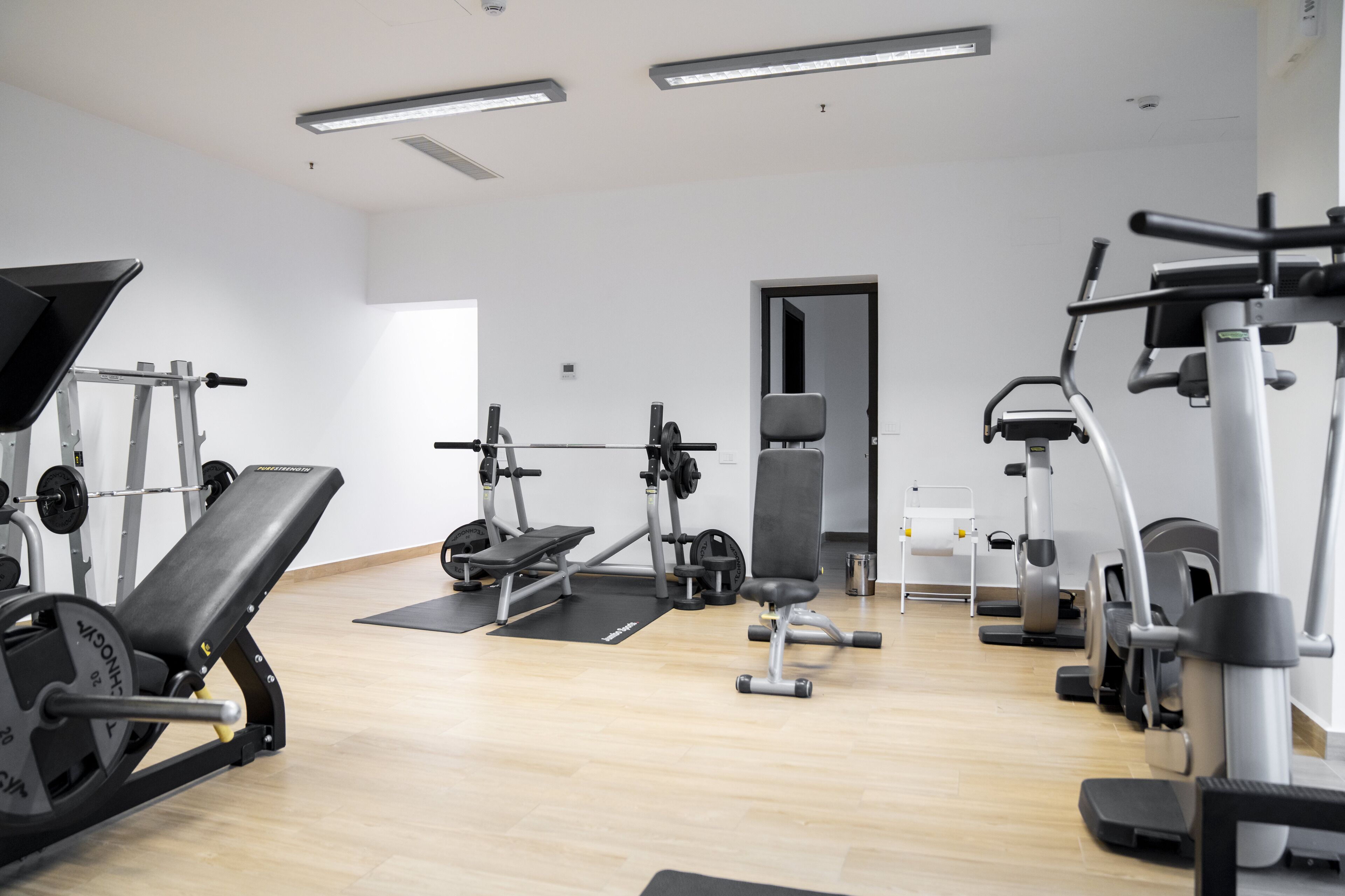 Un gimnasio con diversos equipos de ejercicio, que incluye una prensa de banca, banco de pesas y máquinas de cardio.