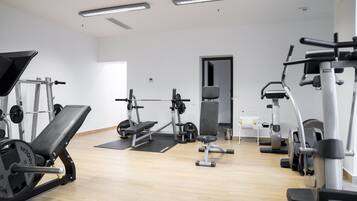 A gym with various exercise equipment, including a bench press, weight bench, and cardio machines.