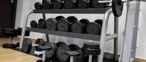 A rack of dumbbells with weights ranging from 16 to 28 pounds, positioned in a gym with a wooden floor and a weight machine in the background.