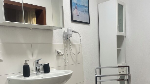 Une salle de bain moderne avec un lavabo blanc, un miroir et un meuble, un sèche-cheveux et un tapis noir sur le sol.