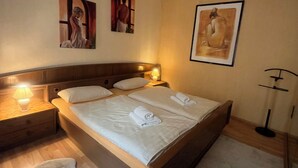 Quarto com cama de madeira, duas mesas de cabeceira com abajures e três obras de arte emolduradas na parede.
