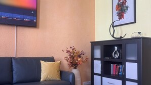 Sala de estar com um sofá preto, uma mesinha de centro, uma estante de livros, uma televisão de tela plana e um quadro na parede.