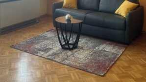 Uma sala de estar com sofá, mesa de centro, televisão de tela plana na parede, radiador e janela com cortinas.