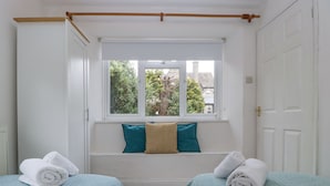 A bedroom with two beds, a window with a view of trees, and a door. - Spring Cottage (Gloucester)