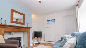 A living room with a fireplace, a television, a sofa, and a painting on the wall. - Spring Cottage (Gloucester)