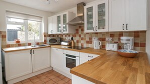 A modern kitchen with white cabinets, a wooden countertop, and a tiled backsplash. - Spring Cottage (Gloucester)