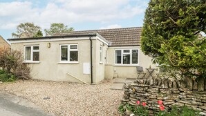 A single-story house with a tiled roof, a gravel driveway, and a stone wall with red flowers. - Spring Cottage (Gloucester)
