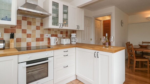 A modern kitchen with white cabinets, a built-in oven, a coffee maker, and a wine bottle. - Spring Cottage (Gloucester)