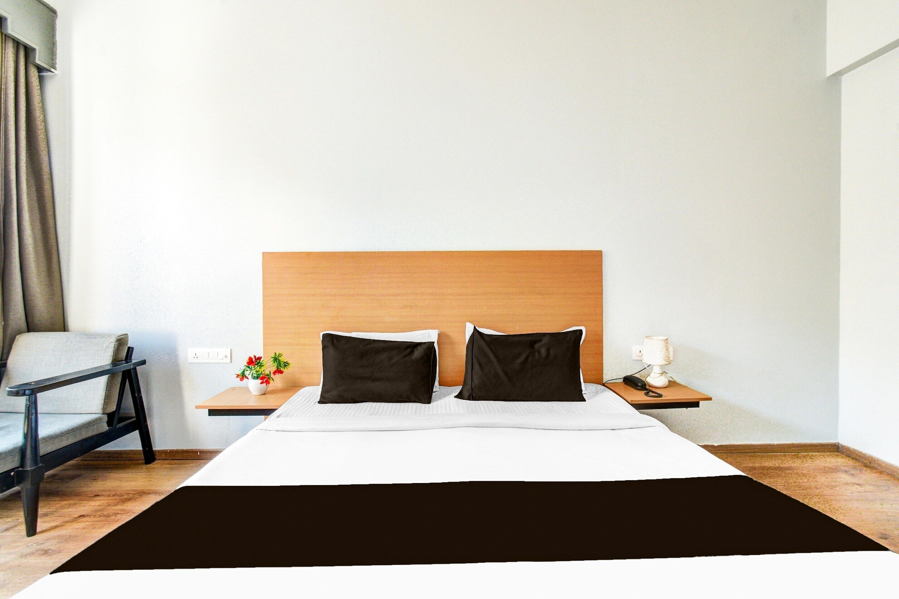 A hotel room with a bed, a nightstand, a chair, and a small table with a plant.