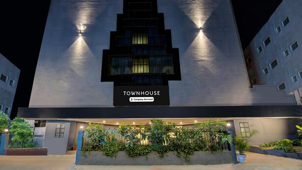 A modern building with a sign reading "TOWNHOUSE" and "Company-Serviced." It features a prominent entrance with a well-lit facade and a landscaped area with plants. - Classic Lakdi Ka Pul (Hyderabad)