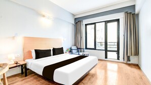 A hotel room with a large bed, a desk with a lamp, a chair, a window with curtains, and a view of the outside. - Classic Lakdi Ka Pul (Hyderabad)