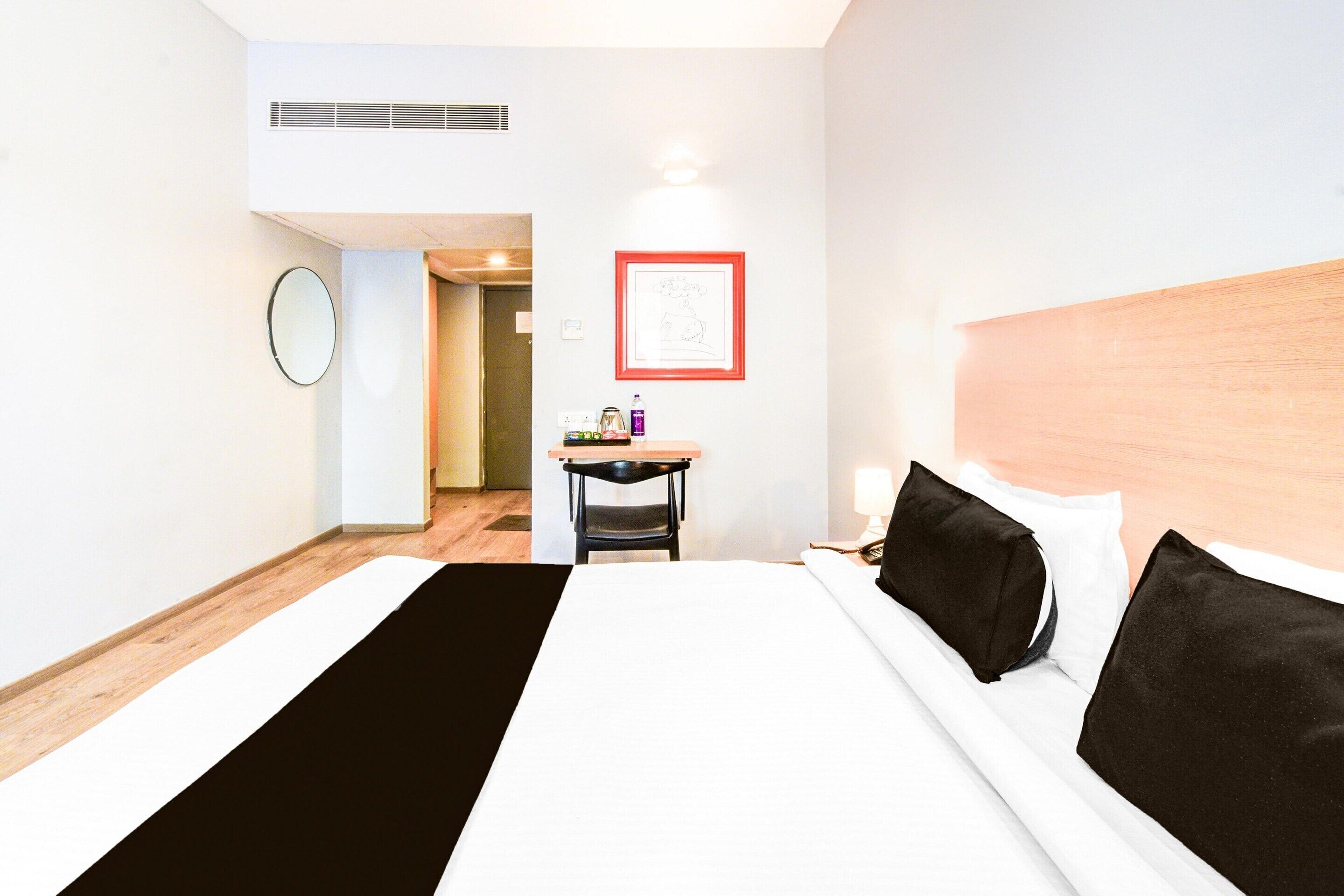 Hotellihuone, jossa on suuri sänky, työpöytä, tuoli, seinällä oleva kehystetty kuva ja ovi, joka johtaa toiseen huoneeseen.