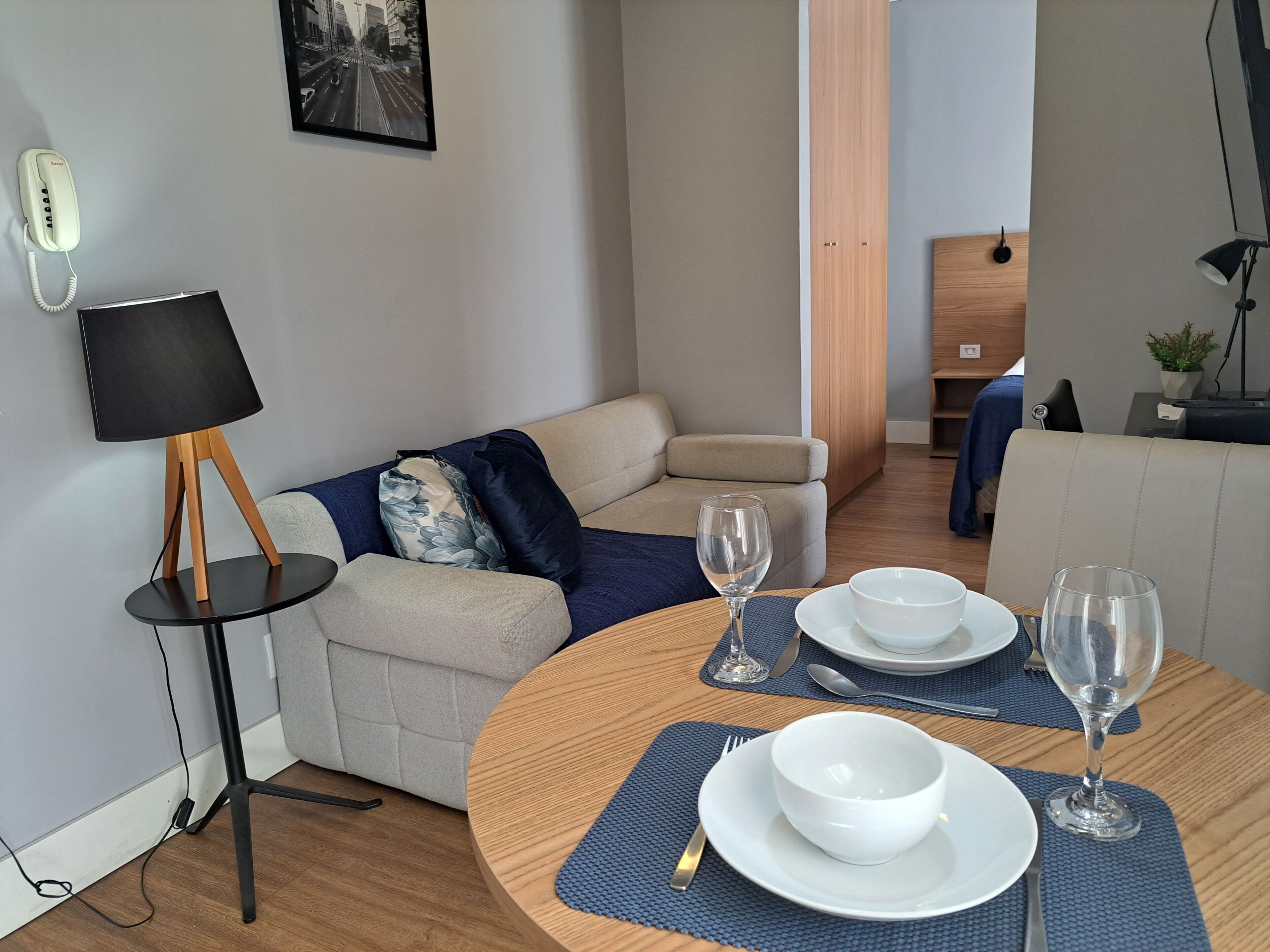 A modern living room with a round wooden table set for dining, a sofa, a lamp, and a framed picture on the wall.