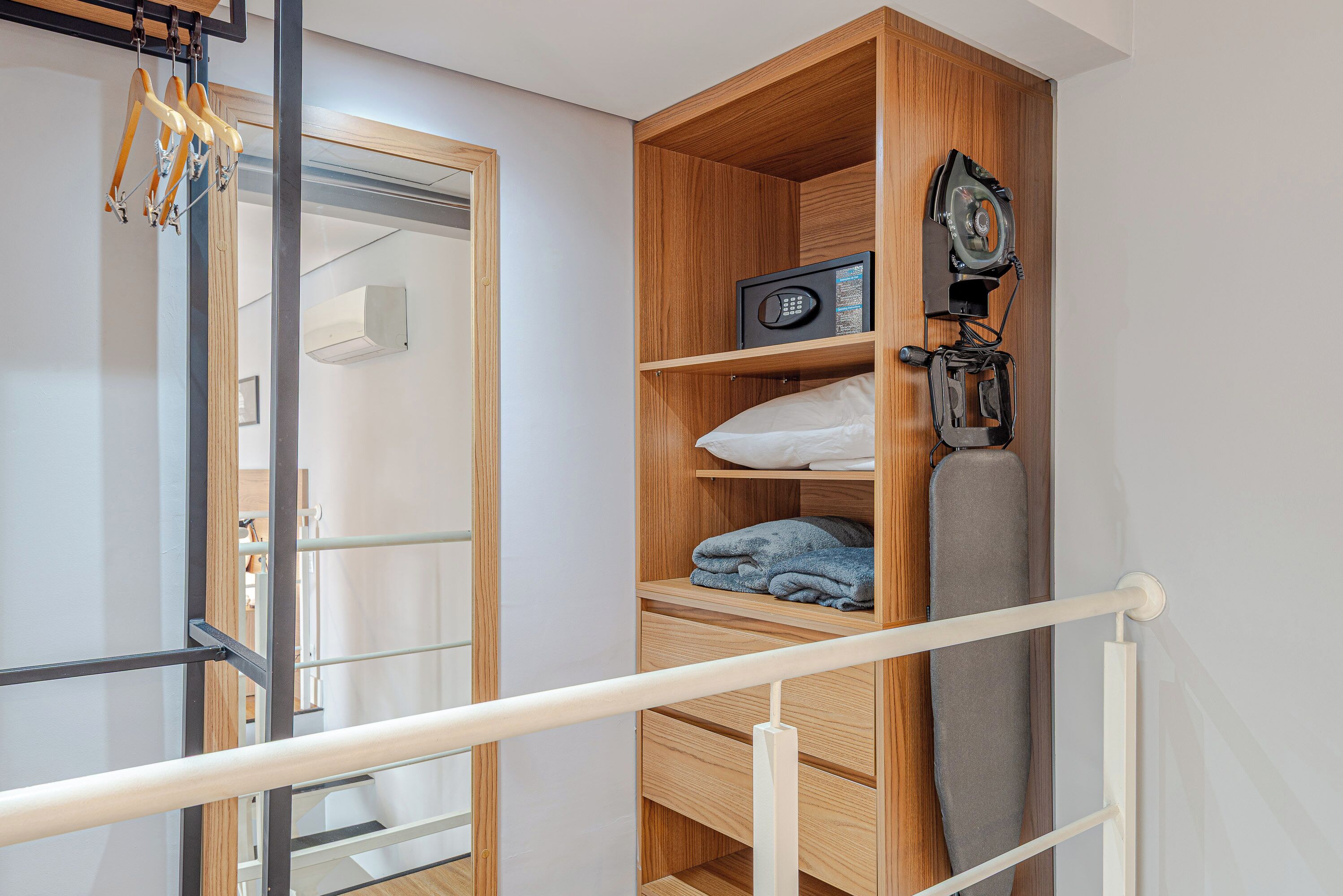 Una habitación con una estantería de madera, un microondas y un perchero con ropa.