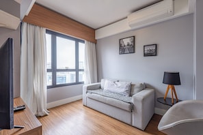 Ett modernt vardagsrum med en soffa, en tv, en lampa och ett fönster med gardiner.