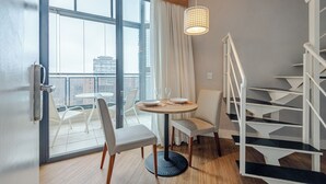 Une chambre d’hôtel moderne avec un balcon, une table de salle à manger ronde entourée de chaises, un escalier et un luminaire suspendu.