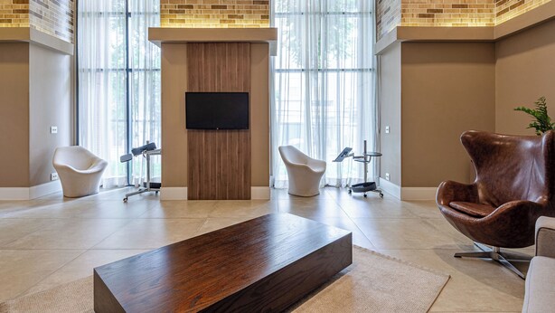Un hall d’entrée moderne avec un grand comptoir de réception en bois, deux fauteuils blancs, un fauteuil en cuir marron et une grande fenêtre donnant sur des arbres.