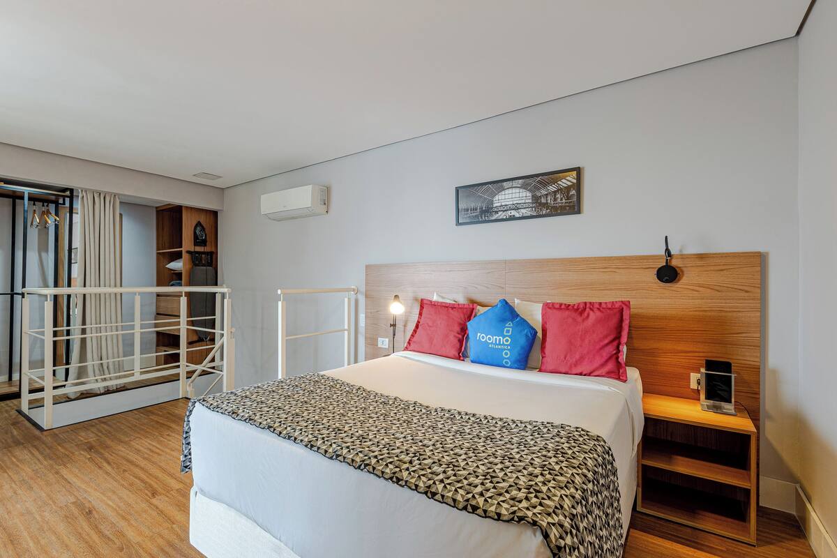Hotellihuone, jossa on sänky, yöpöytä, vaatekaappi ja ikkuna, jossa on verhot.