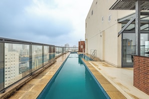 En pool på taket, avgränsad av en glasvägg, med en tegelvägg och utsikt över stadens byggnader.