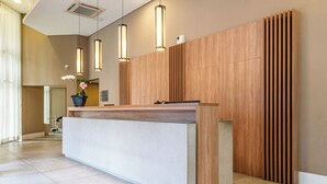 Un comptoir d’accueil avec un dessus de couleur claire, un lambris en bois sur le mur et des luminaires suspendus.