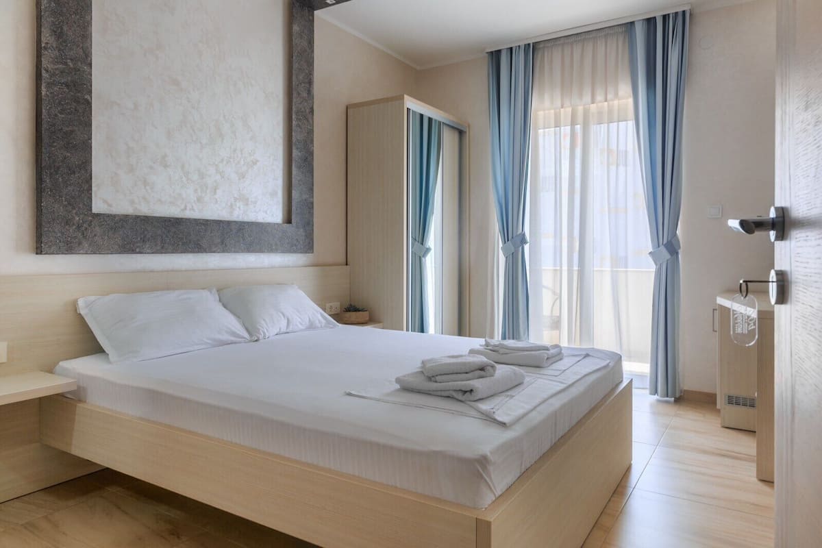 A modern hotel room with a large bed, a bedside table, a small plant, and a view of the outdoors through the window.