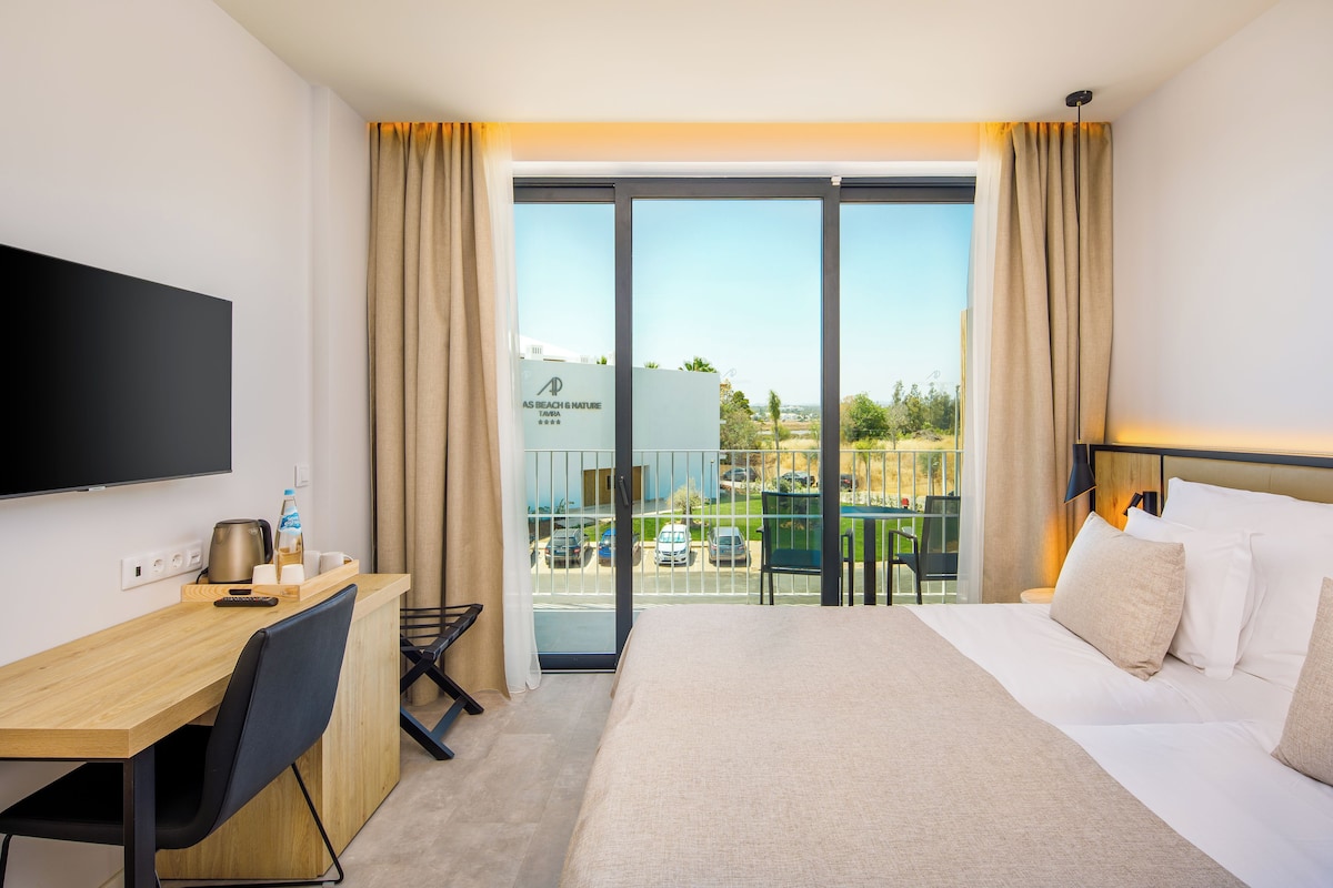 A hotel room with a bed, a desk, a chair, a TV, and a balcony with a view of the outside.