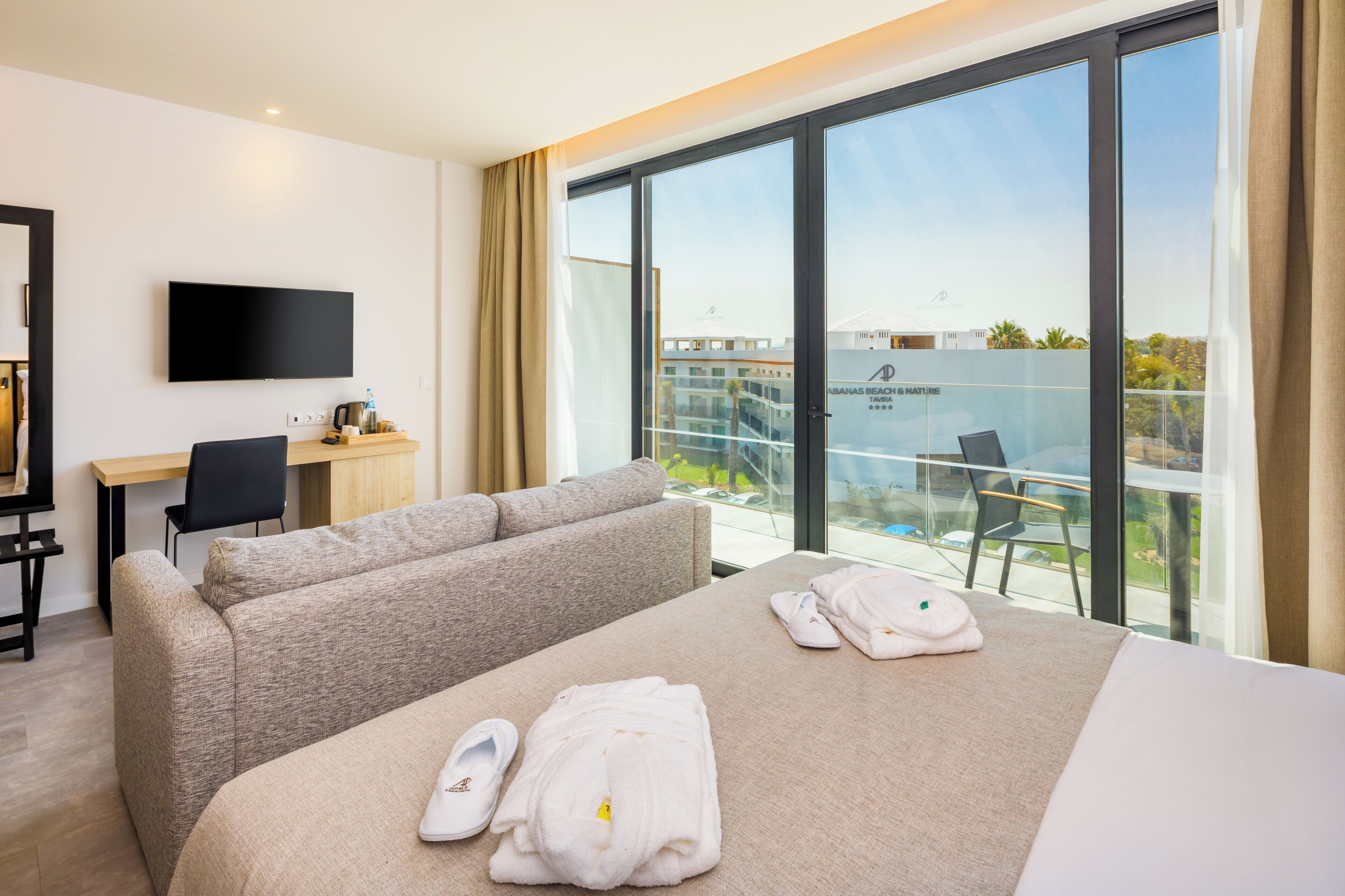 Ein Hotelzimmer mit Bett, einer Couch, einem Schreibtisch, einem Fernseher und einem Balkon mit Blick.